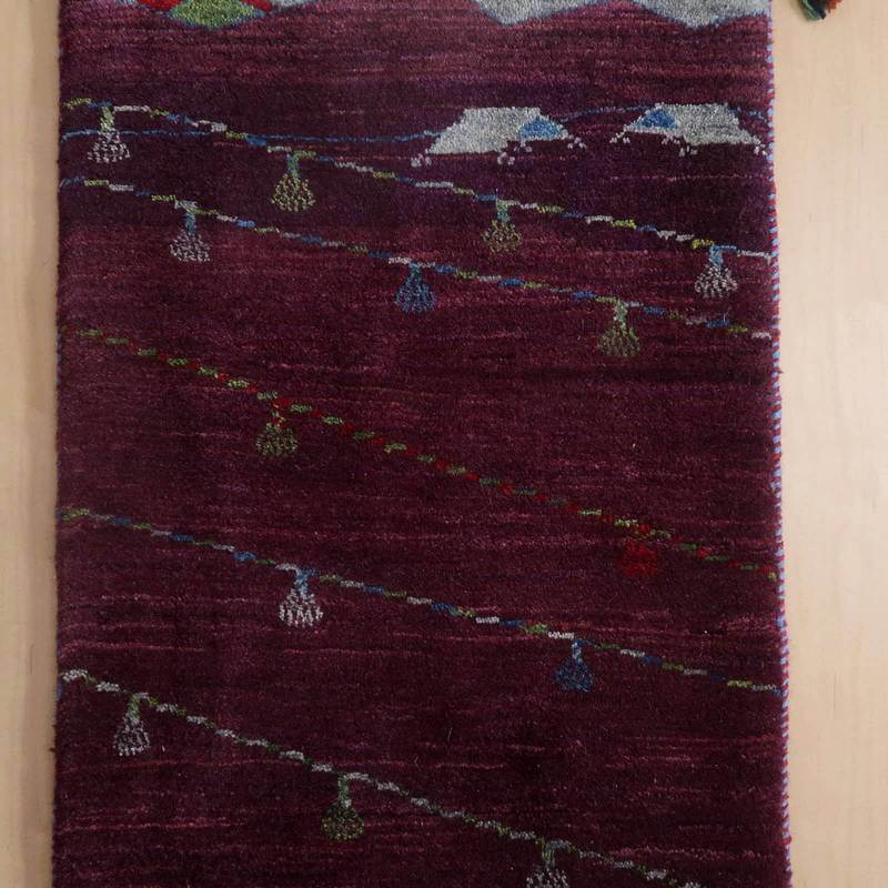 深い赤紫の色調に、手織りのギャッベ特有の繊細な模様が浮かび上がるウールラグが敷かれている。