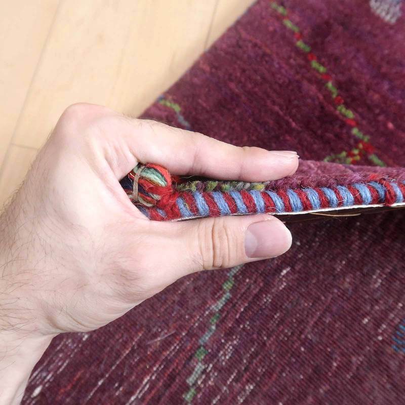 手に持たれたギャッベラグの厚みと鮮やかな色合いが際立ち、ウールの手織り模様が丁寧に編み込まれているのが見える。