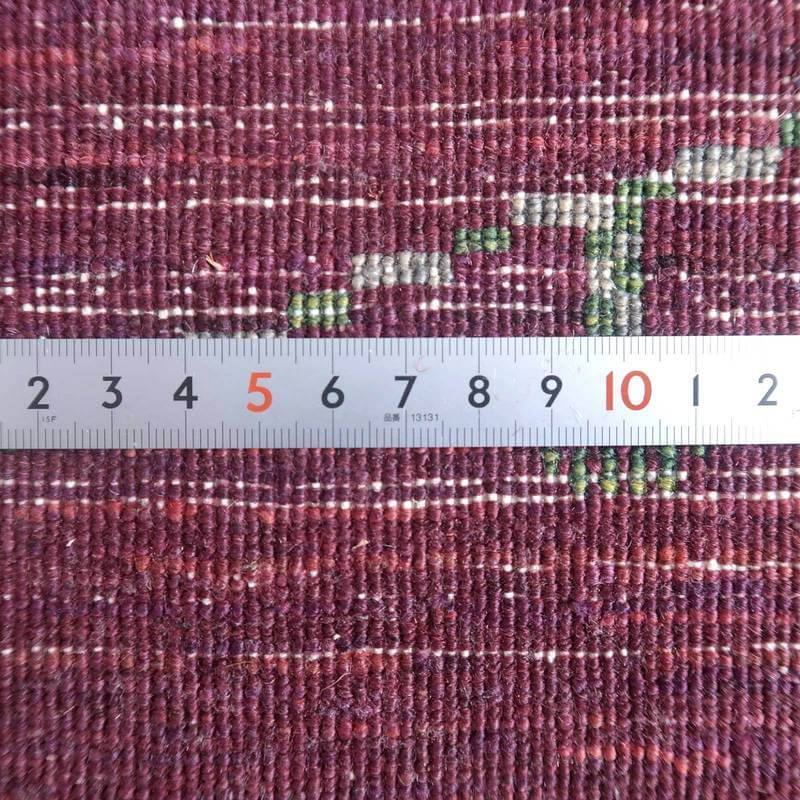 深みのある紫色の手織りウールギャッベの繊細な織り目と模様が定規と共に詳細に映し出されている。