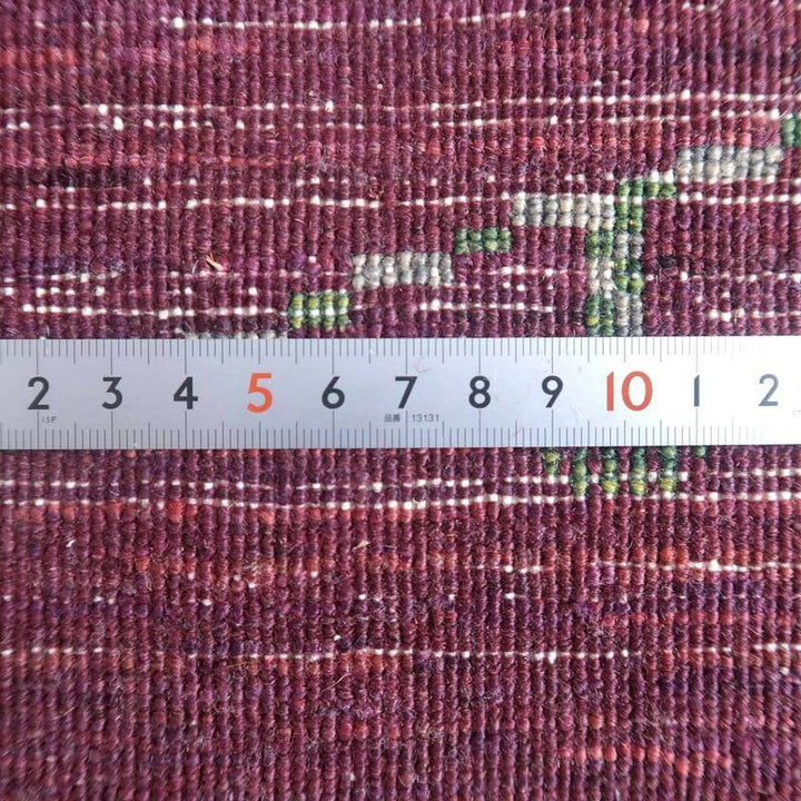 深みのある紫色の手織りウールギャッベの繊細な織り目と模様が定規と共に詳細に映し出されている。