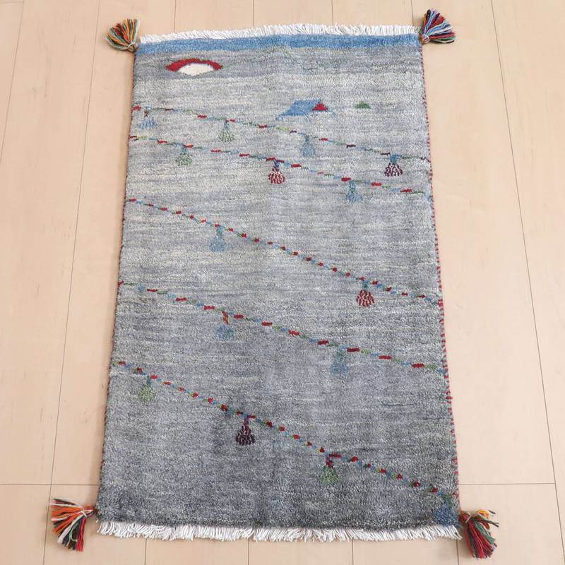 ギャッベ／ルリバフ 85×54cm（HSS-71707）は、グレーを基調に色とりどりの模様が施された手織りのギャッベラグが、温かみあるウールの質感と共に木目の床に敷かれている。