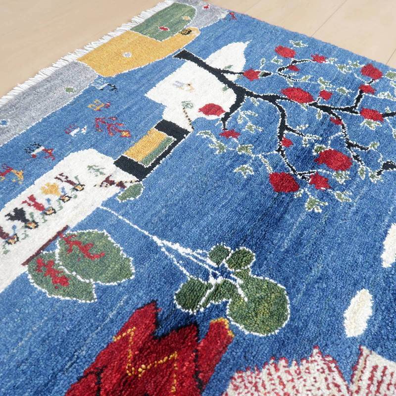 青を基調に赤や緑の模様が丁寧に手織りされたギャッベのウールラグが、木目の床に敷かれている。