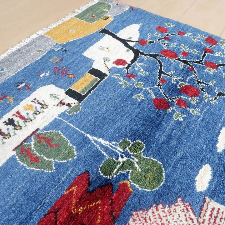 青を基調に赤や緑の模様が丁寧に手織りされたギャッベのウールラグが、木目の床に敷かれている。