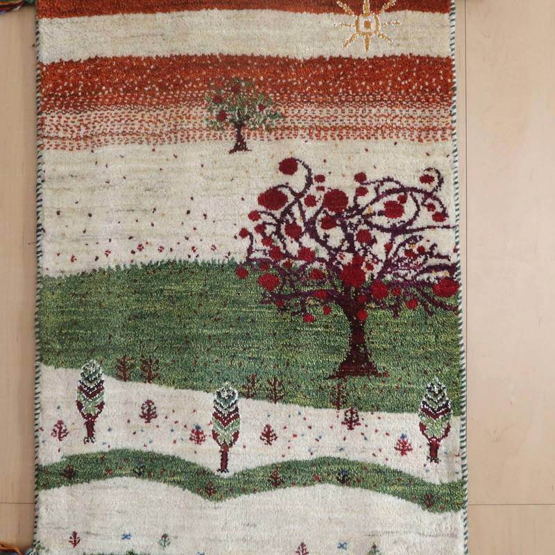 色鮮やかな樹木と自然の風景が描かれた手織りのギャッベラグが、ウール素材の温かみある質感で床に美しく敷かれている。