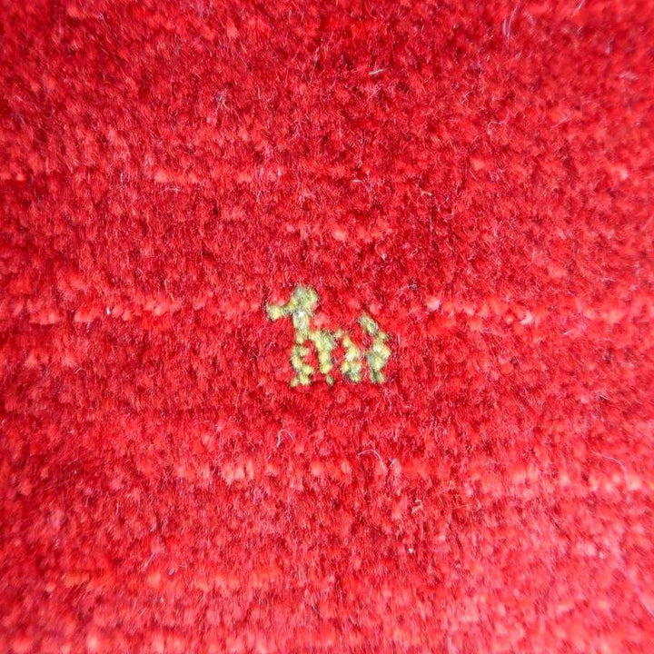 赤い手織りギャッベのラグに描かれた小さな緑色の動物モチーフが、ウールの質感とともに繊細に浮かび上がっています。