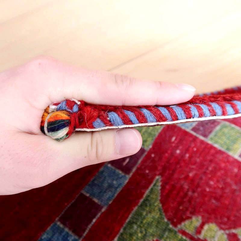 手織りのウールで丁寧に作られたペルシャ絨毯のギャッベが、鮮やかな赤と青のストライプ模様が際立つ厚みとぬくもりを感じさせる断面から見える。