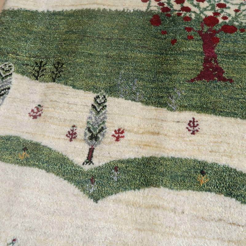 手織りのギャッベラグが、緑豊かな風景と赤い木々を織り込んだウール素材で、ペルシャ絨毯専門店の通販で入手可能な美しい一枚が床に広がっている。