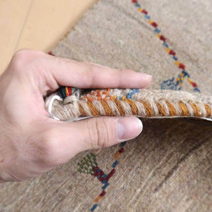 手織りのギャッベラグの縁を持ち上げ、ウールの柔らかさと丁寧に織られた模様の繊細さが際立っている。