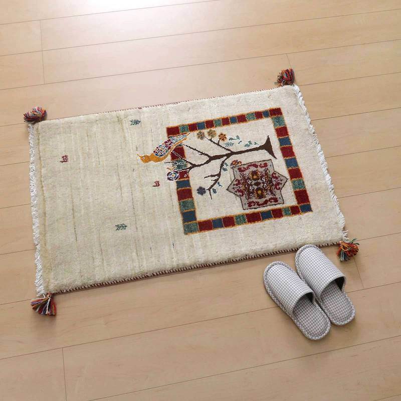 木目の床に敷かれたペルシャ絨毯専門店の手織りギャッベラグは、鳥と木の温かみあるデザインが彩りを添えている。