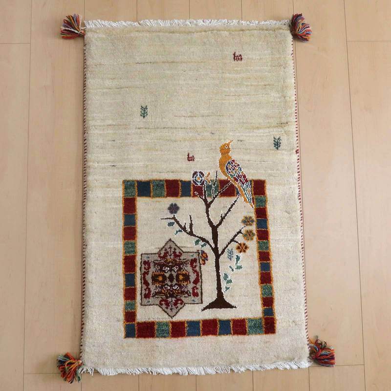 ギャッベ／ルリバフ 94×60cm（HSS-71779）は、手織りウールのギャッベラグが床に敷かれ、ペルシャ絨毯専門店の通販で購入できる、鳥と木のモチーフが温かみを添えている。