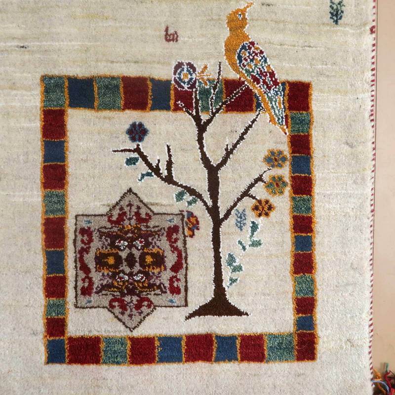 手織りのウール素材で丁寧に仕上げられたペルシャ絨毯専門店のギャッベラグには、カラフルな鳥と木のモチーフが描かれている。