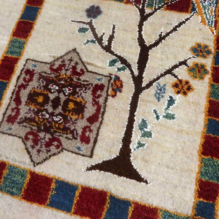 手織りのペルシャ絨毯が織り出す、温かみのある木と花の模様が際立ち、ウール素材の柔らかさが伝わるギャッベラグが見える。