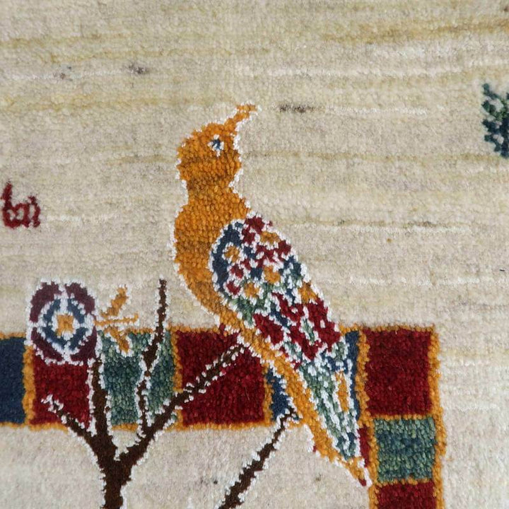 手織りのウールギャッベに描かれた鮮やかな鳥のデザインが精緻なペルシャ絨毯の一部として際立っている。