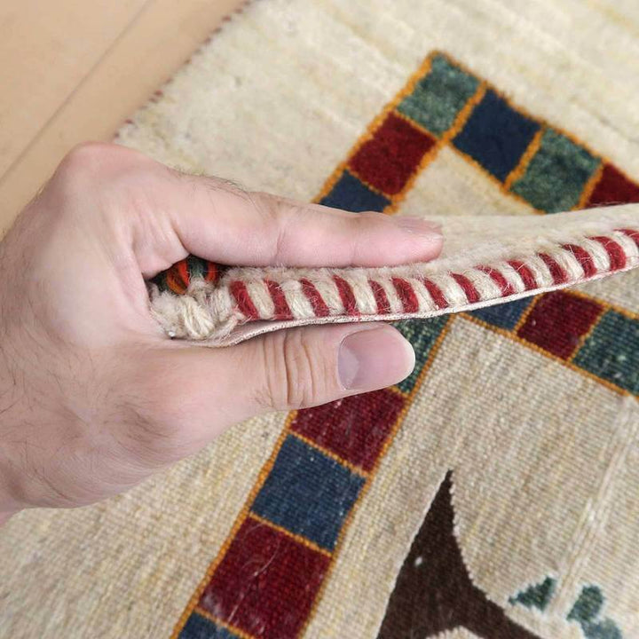 手織りのウール製ギャッベラグの厚みを指で持ち上げることで、繊細なペルシャ絨毯の縁取りと模様が際立っている。