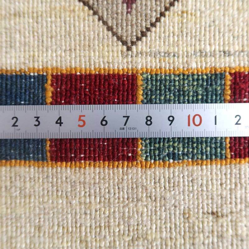 手織りのギャッベラグの繊細なウールの織り目が、定規とともに赤や緑の模様の鮮やかさを引き立てている。