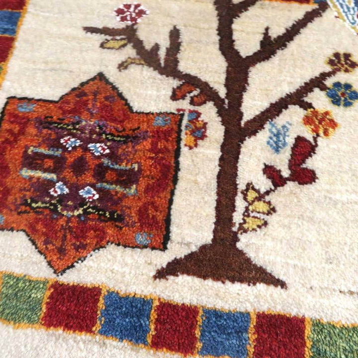 手織りのウール製ギャッベラグが、ペルシャ絨毯専門店の通販で購入可能な一枚として、色鮮やかな花や木のモチーフが温かみを感じさせるデザインで際立っている。