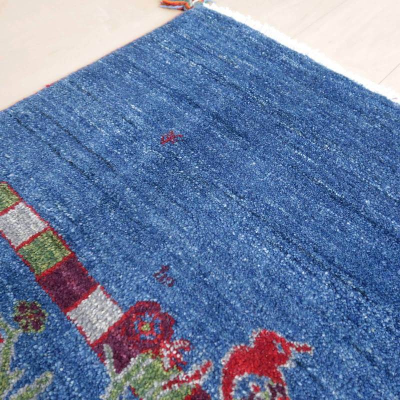 深みのある青色のウールで手織りされたギャッベラグが床に広がり、ペルシャ絨毯の専門店で通販可能な美しい模様が際立っている。