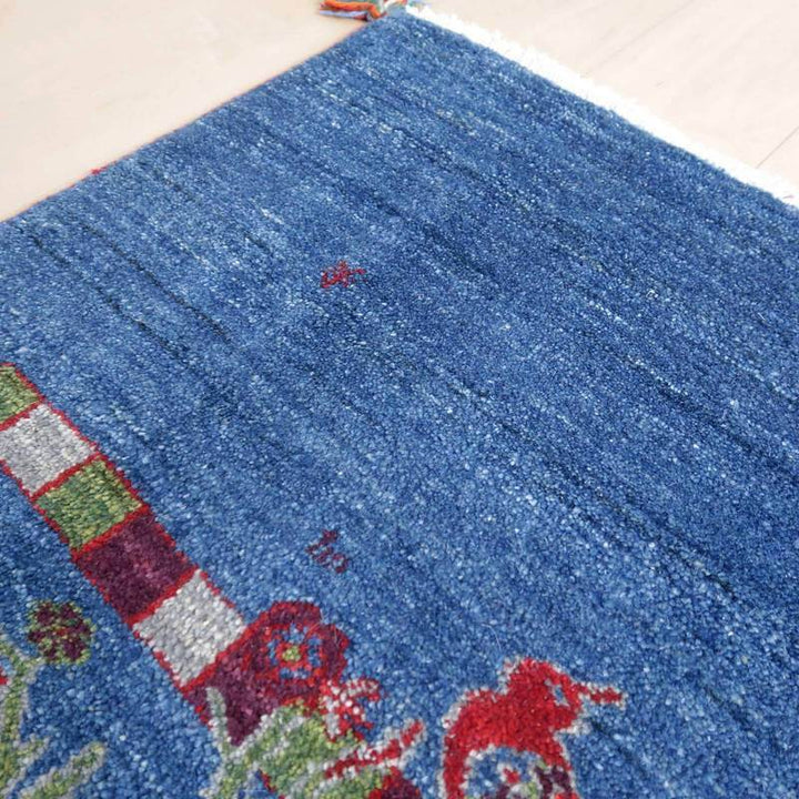 深みのある青色のウールで手織りされたギャッベラグが床に広がり、ペルシャ絨毯の専門店で通販可能な美しい模様が際立っている。