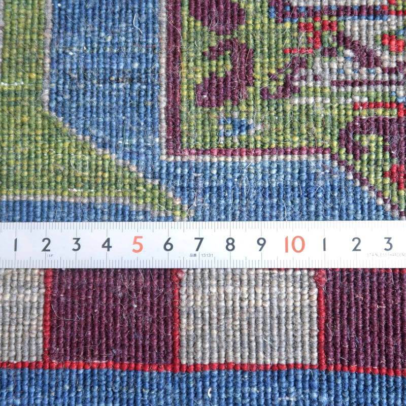 カラフルな模様が魅力的な手織りのウール製ギャッベラグが、定規との比較でその織りの緻密さが際立っている。