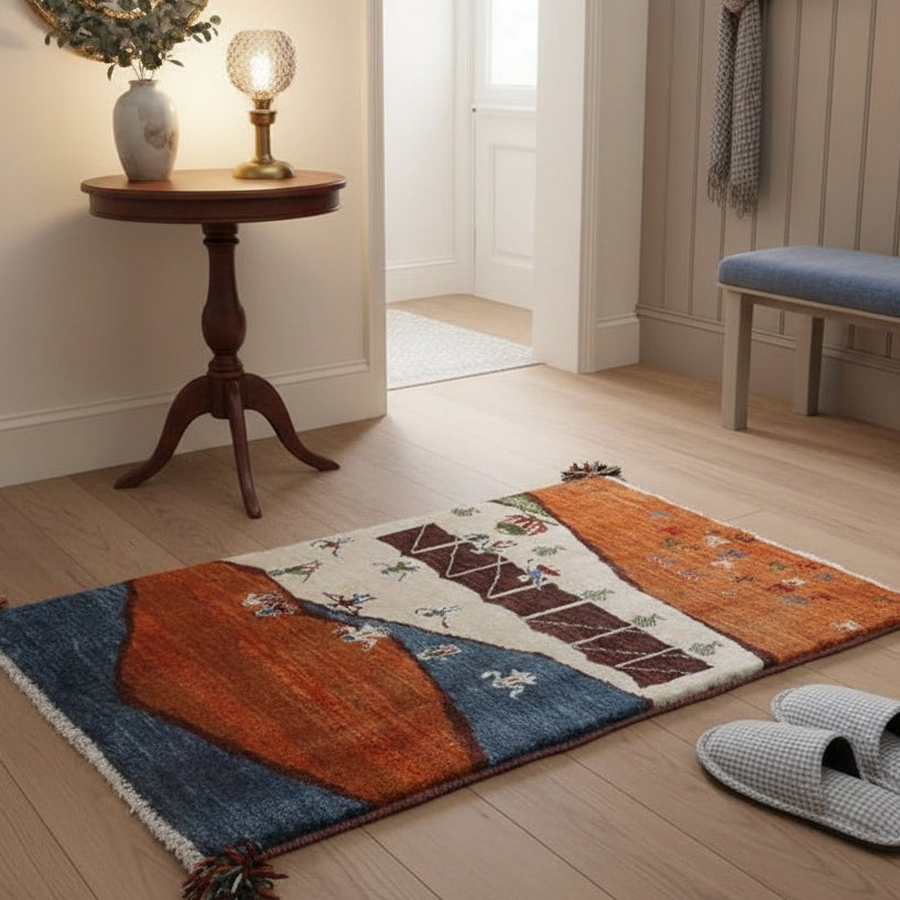 温かみのあるオレンジとブルーの手織りギャッベラグが、スリッパと共にナチュラルな床の上に置かれている。