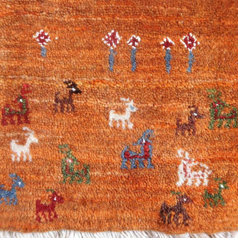 鮮やかなオレンジ色のペルシャ絨毯に、手織りの可愛らしい動物柄と花模様が描かれており、ギャッベラグの温かみが際立っている。