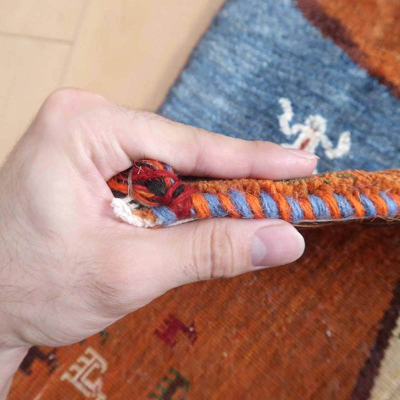 手に取られたギャッベラグの厚みが感じられるこの一枚は、ウール素材の手織りの繊細さと温かみを伝え、ペルシャ絨毯専門店ならではの品質が際立っている。