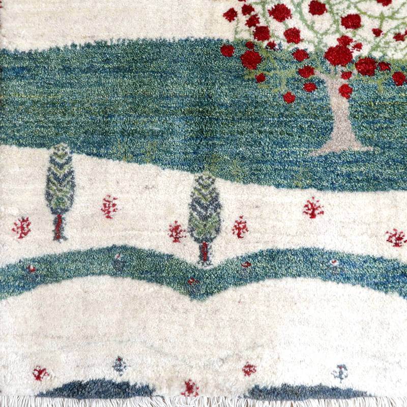 色鮮やかな赤い木と緑の風景が描かれた手織りのウール製ギャッベラグが、ペルシャ絨毯専門店の通販で入手可能な一枚。