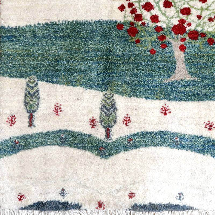 色鮮やかな赤い木と緑の風景が描かれた手織りのウール製ギャッベラグが、ペルシャ絨毯専門店の通販で入手可能な一枚。