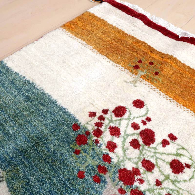 赤い花模様が鮮やかに描かれた手織りのギャッベラグは、ウールの質感とペルシャ絨毯の伝統が調和し、床に温かみを添えている。