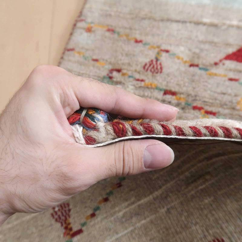 手に取られたギャッベラグの厚みが際立ち、手織りのウール素材の密度と色彩豊かなペルシャ絨毯の模様が見える。