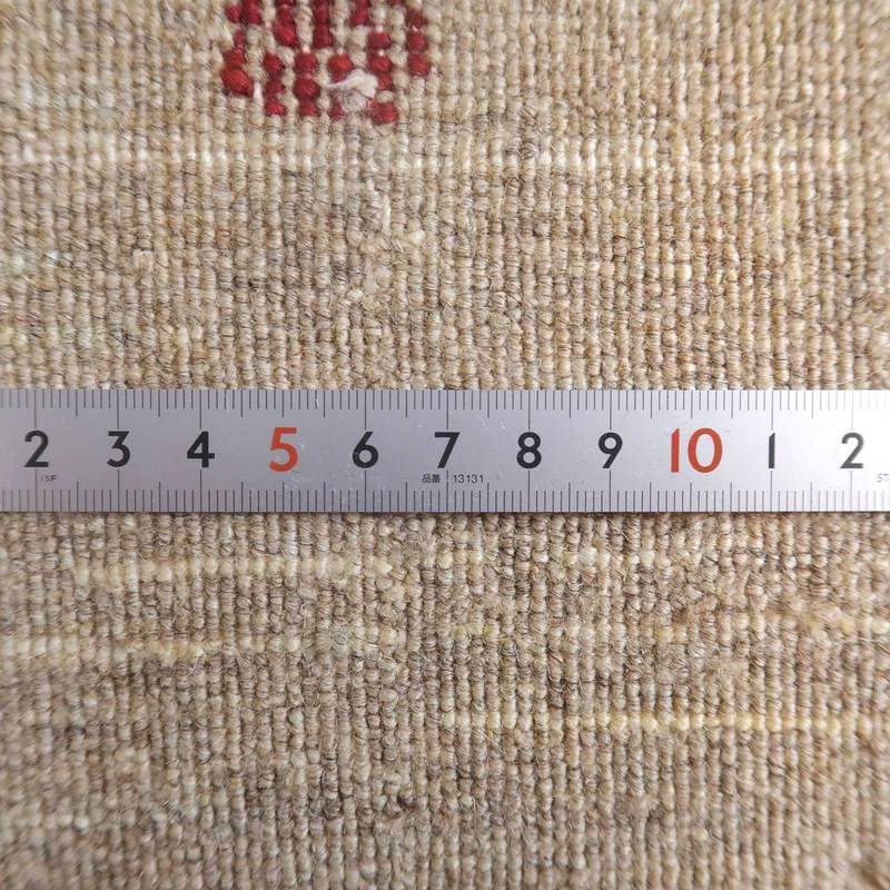 手織りのギャッベラグの細やかな織り目が定規と共に捉えられており、ウールの暖かさと優しい色合いが際立っている。