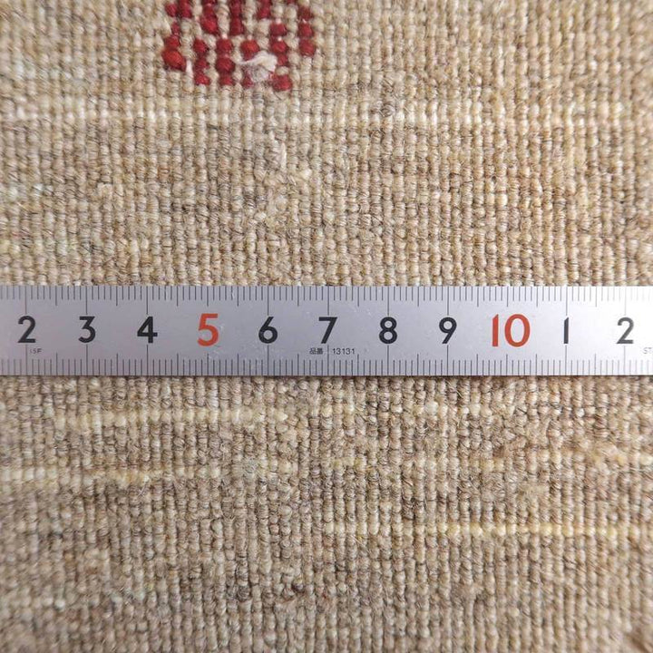 手織りのギャッベラグの細やかな織り目が定規と共に捉えられており、ウールの暖かさと優しい色合いが際立っている。