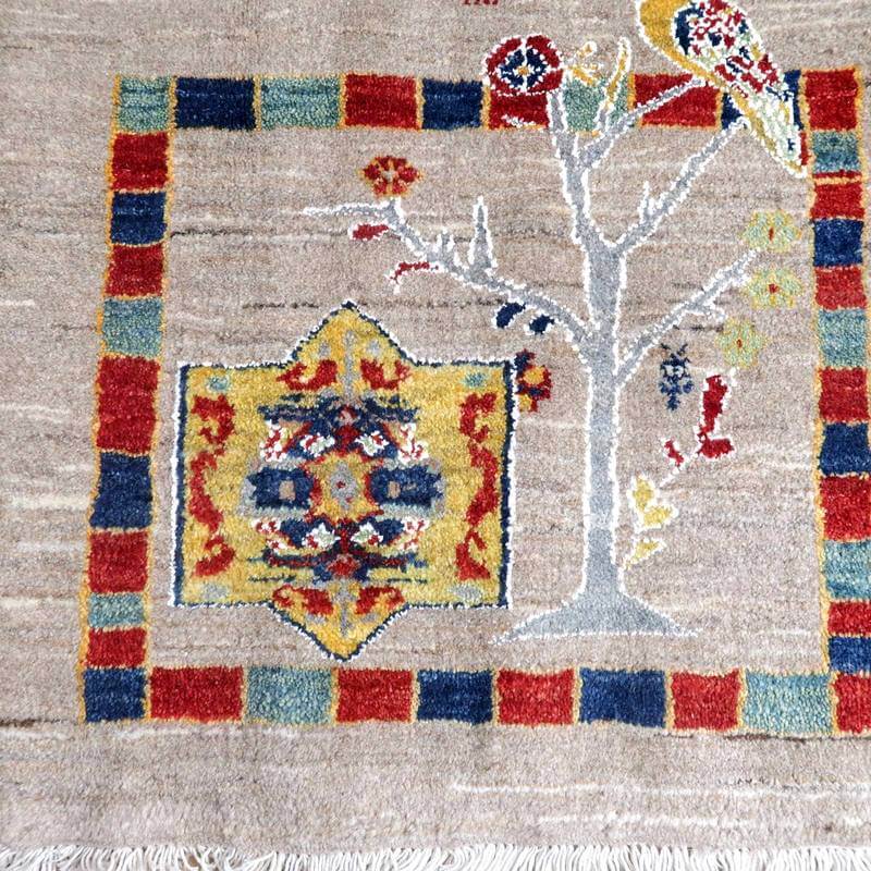 色鮮やかな模様と自然のモチーフが特徴的な手織りウールのギャッベラグが床に敷かれている。