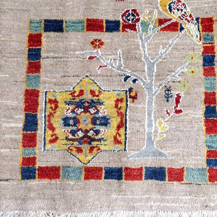 色鮮やかな模様と自然のモチーフが特徴的な手織りウールのギャッベラグが床に敷かれている。