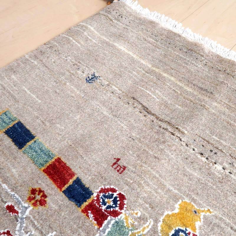 ベージュのウール素材に色鮮やかな模様が織り込まれた手織りのギャッベラグが、床に優しく広がっています。