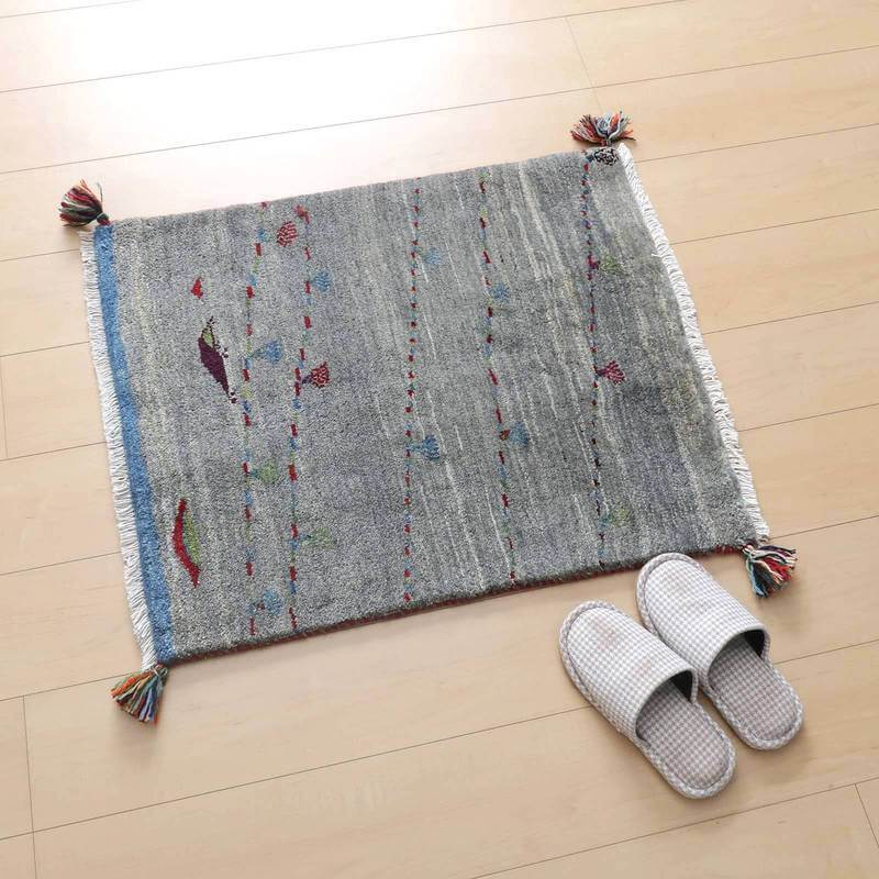 明るい木目の床に置かれた手織りのウール製ギャッベラグが、色とりどりの模様とタッセルでぬくもりを添えている。