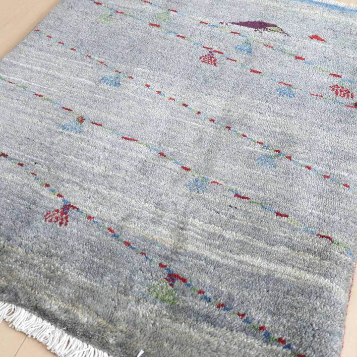 手織りのギャッベラグが優しい色合いのグレーを基調に、赤や青の模様がアクセントとして散りばめられたデザインが床に広がっている。