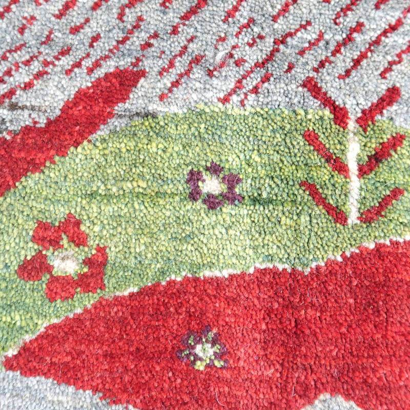 手織りのペルシャ絨毯専門店から通販できるギャッベラグの接写画像で、赤と緑のウール素材の織り目に花模様が丁寧に施されている。
