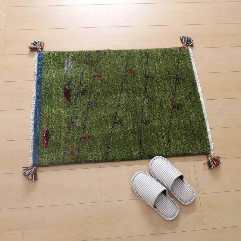 緑豊かな手織りウールのギャッベラグが明るい木目の床に敷かれ、色とりどりのタッセルがアクセントとなっている。