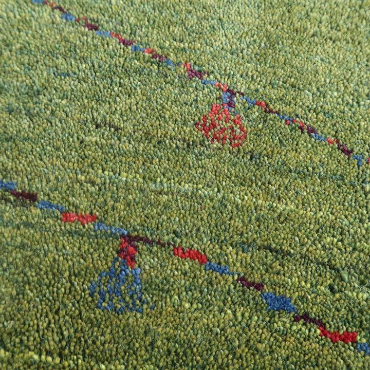 緑色のウール素材に赤と青の模様が丁寧に手織りされたギャッベのラグが、ペルシャ絨毯専門店の通販で購入できる。