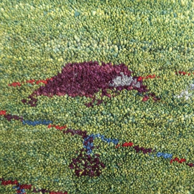 緑の背景に赤い模様が浮かび上がる手織りのギャッベラグが、ウールの温かみを感じさせる質感で描かれている。