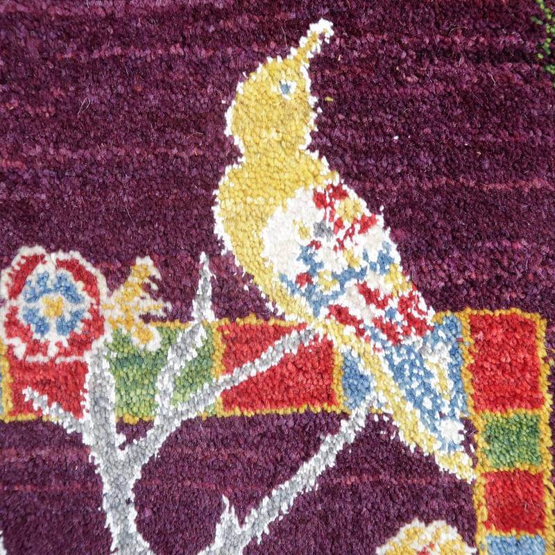 紫色の地に黄色と赤の鳥が鮮やかに描かれた手織りのギャッベラグが、丁寧なウール素材の織り目の中に色鮮やかに映えている。