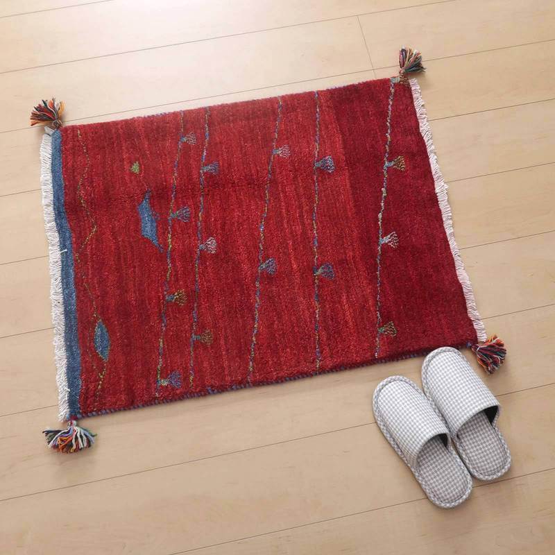 赤い手織りのギャッベラグが明るい床に敷かれ、繊細な模様とウールの柔らかさが際立っている隣にはスリッパが置かれている。