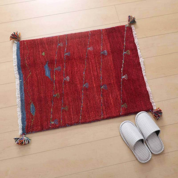赤い手織りのギャッベラグが明るい床に敷かれ、繊細な模様とウールの柔らかさが際立っている隣にはスリッパが置かれている。