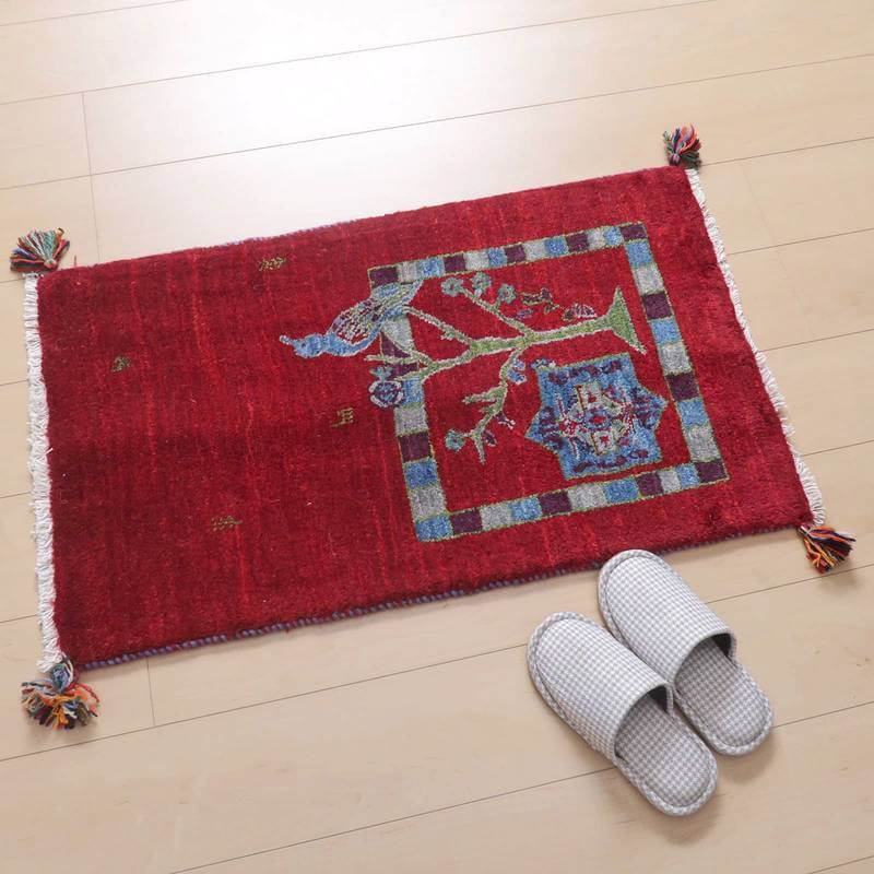 鮮やかな赤い手織りのギャッベラグが、ウールの温かみを感じさせるデザインで床に敷かれ、ペルシャ絨毯専門店の通販商品として魅力が際立っている。