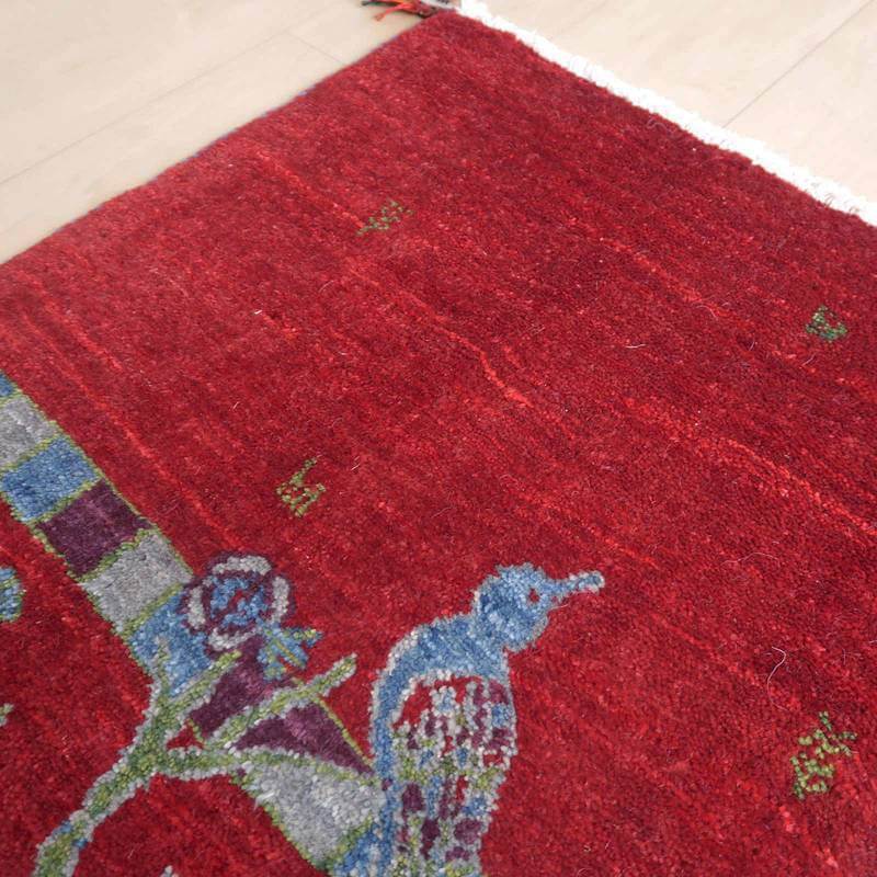 赤い色合いが印象的な手織りのギャッベが床に広がり、ペルシャ絨毯の伝統的な模様が際立っている。