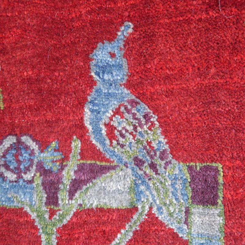 鮮やかな赤の背景にブルーの鳥が丁寧に織り込まれたギャッベラグの接写が見える。
