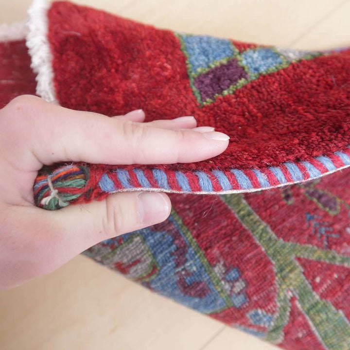 手に持たれたギャッベラグの鮮やかな赤と繊細な模様が、手織りの温かみを感じさせるウール素材の厚みを強調している。