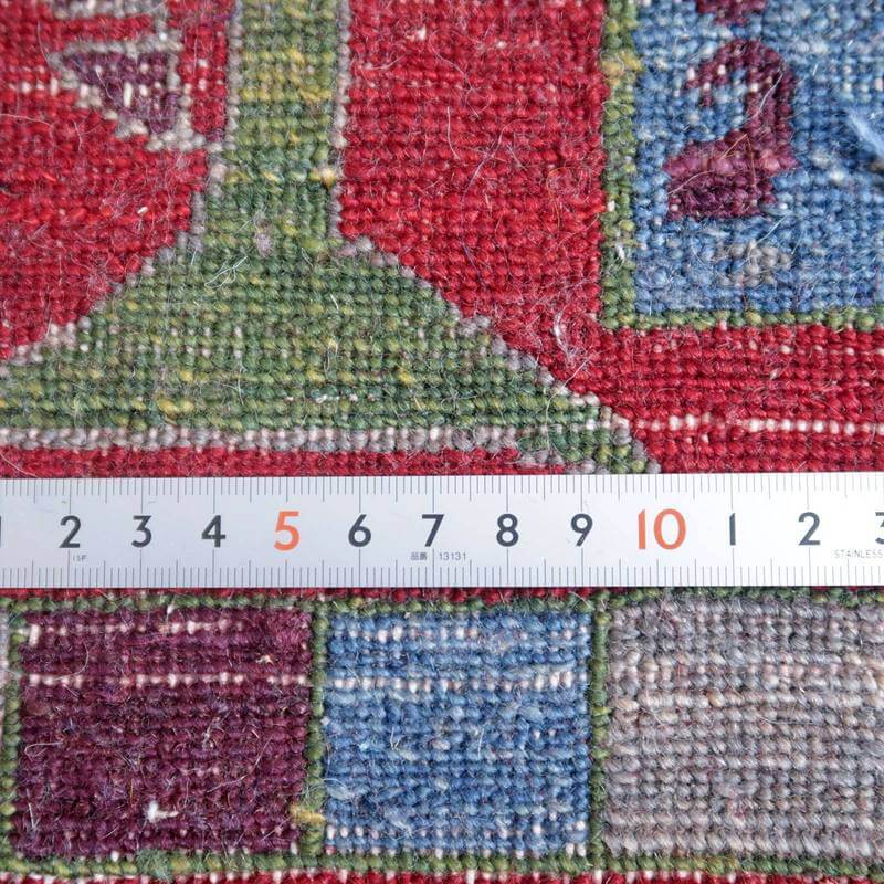 緻密に手織りされたウールのギャッベラグが赤や青の色鮮やかな模様を織り成し、定規と共にその織り目の細かさが際立っている。