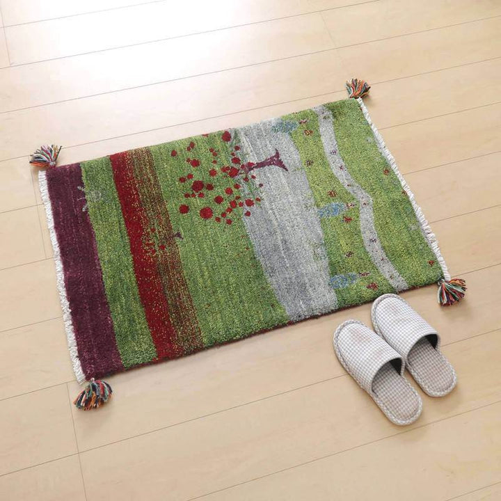 緑と赤の自然な模様が特徴的な手織りのウールギャッベラグが、木目の床に調和しつつスリッパが置かれている。